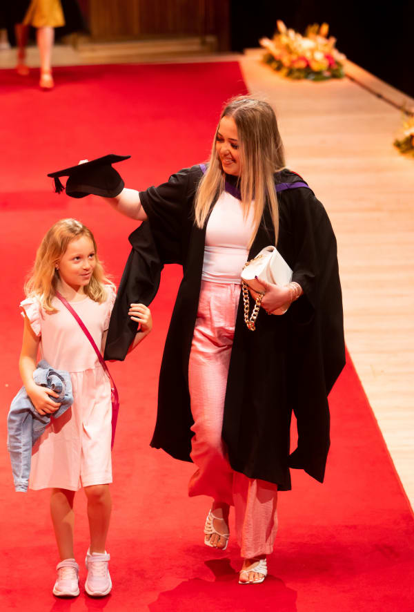 Student walking across stage with a small child who they put their graduation hat on