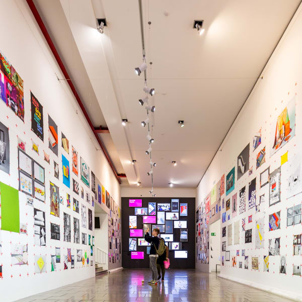 A corridor with both walls covered with artworks and the centre end wall has a digital display.
