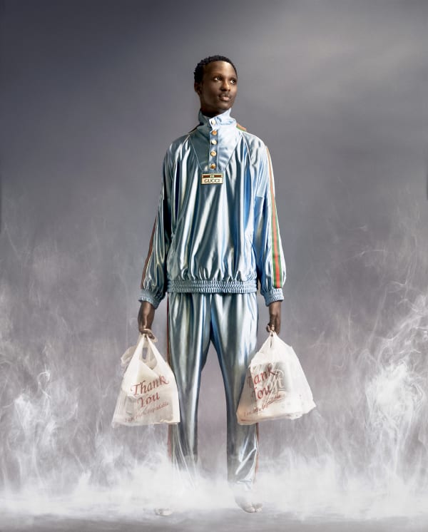 Male model in shiny tracksuit holding grocery bags.