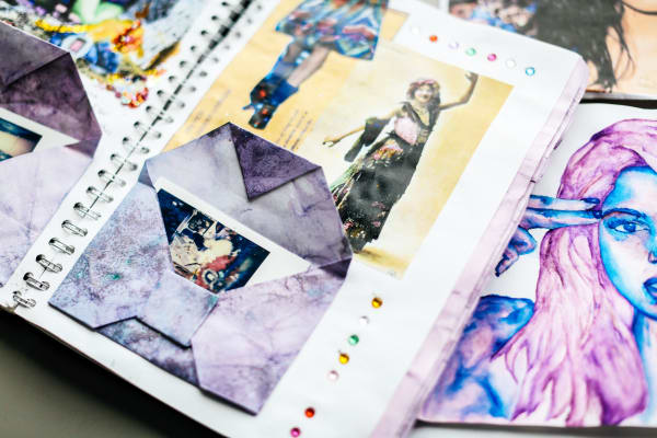 photgraph of a decorative sketchbook with illustrations of people in purple and blur shades.