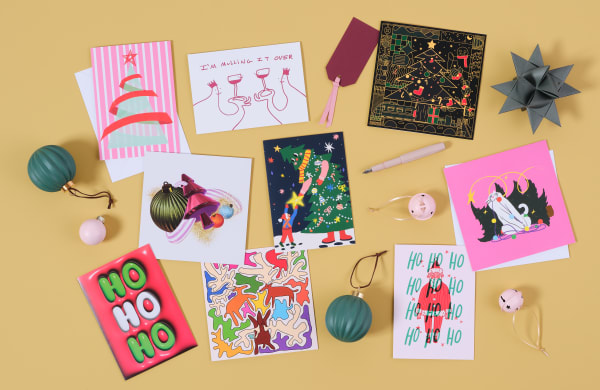 9 Christmas cards are arranged on a yellow background, with green and pink baubles, red present tags and a pink pen.