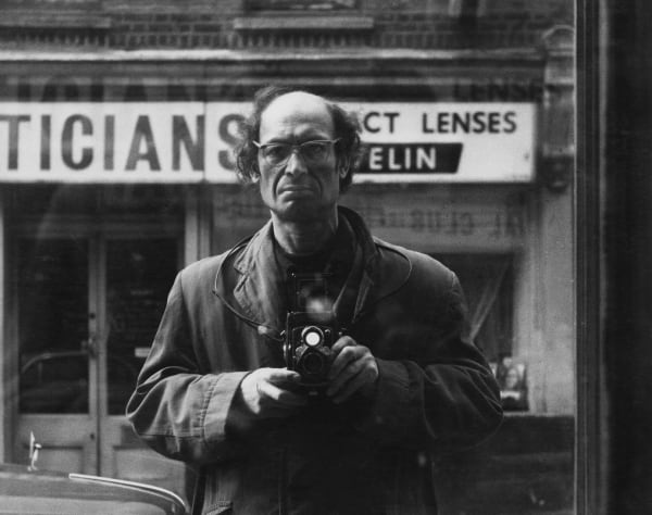Harry Diamond taking a self portrait with a vintage camera, in a window reflection.
