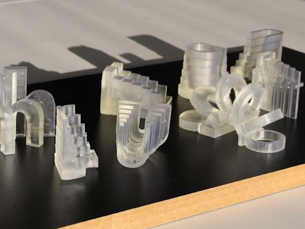 Clear 3D-printed architectural models and shapes displayed on a black work surface in the 3D workshop.