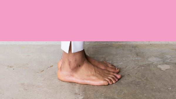 two feet with hem of white trousers stand on concrete, half of the banner is plain pink