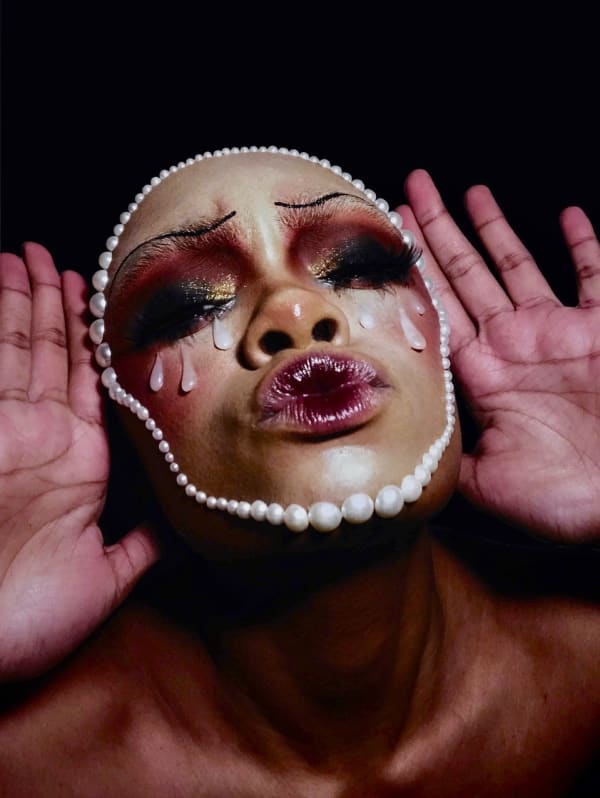 A person with their hands held up either side of their face wearing vivid makeup