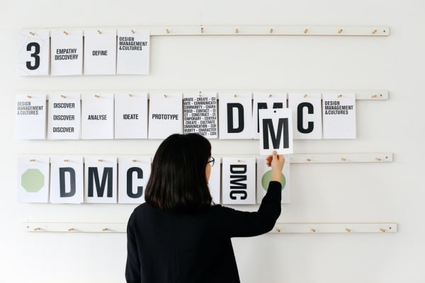 Woman placing cards with letters and numbers on a wall. MA Design Management and Cultures, Ngoc (Sam) Trieu working in the Studio. Copyright holder: Alys Tomlinson