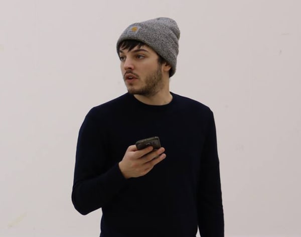 Man in black jumper and dark knitted beanie holding a phone