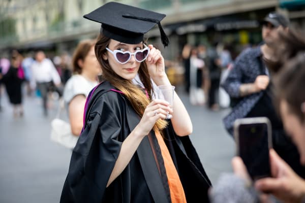 A graduate outside the Southbank Centre wearing their graduation gown and hat and slightly pulling down their white sunglasses