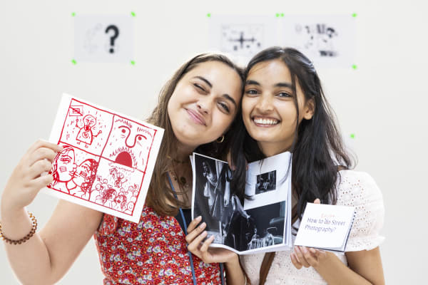 2 students holding up work and smiling