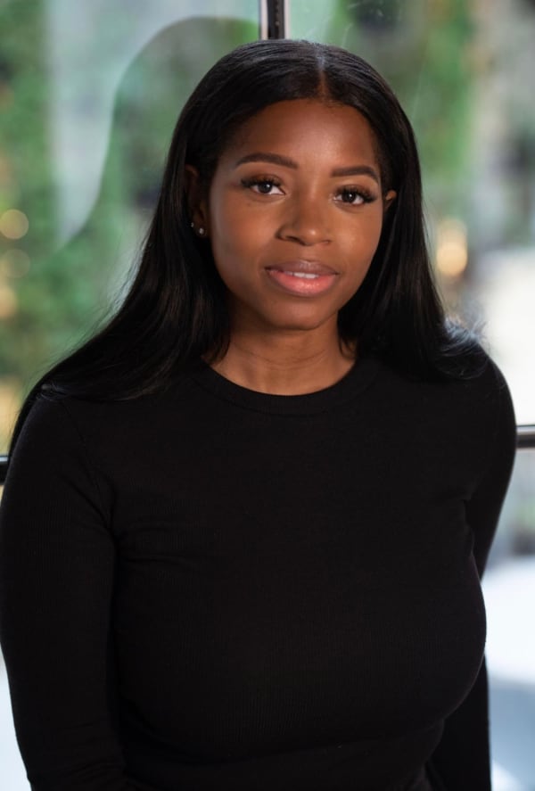 Kamiqua Lake stands in front of a window. Kamiqua has long, dark hair and wears a black top. 