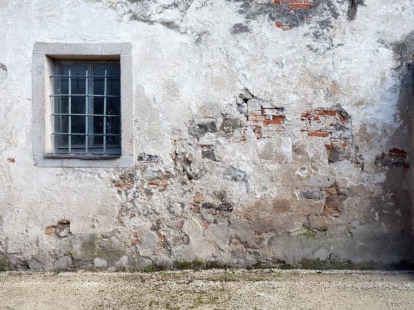 An exterior of an old building, with worn away plaster revealing red bricks beneath.