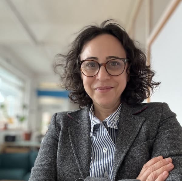 A square head and shoulders shot of Paulina. She is smiling and wearing a blue and white striped shirt, glasses and a grey blazer.
