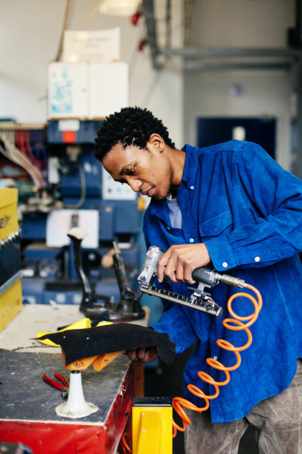 Boy in a workshop using a hot glue gun on a shoe model