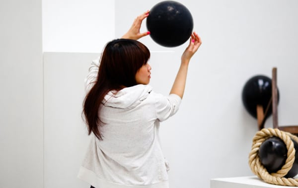 Woman holding a black ball against white wall