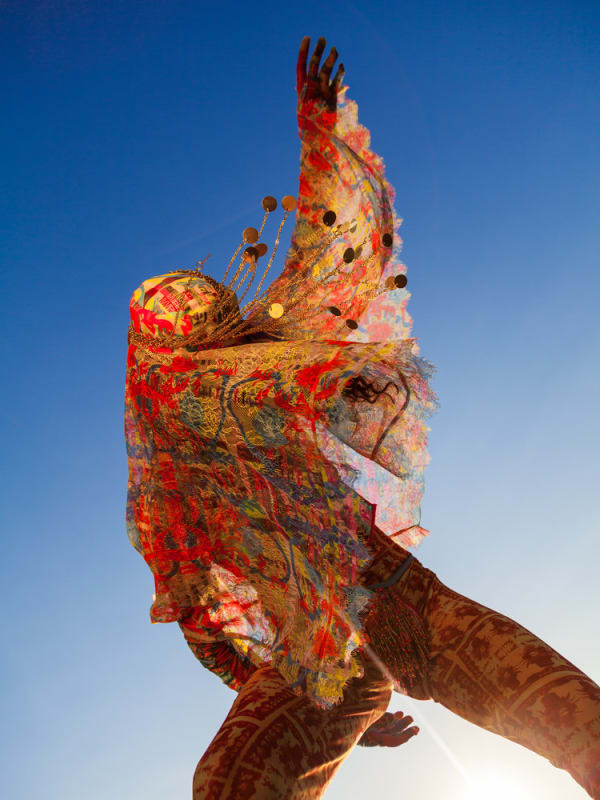 Figure wrapped in colourful scarf stretching arm up into the sky