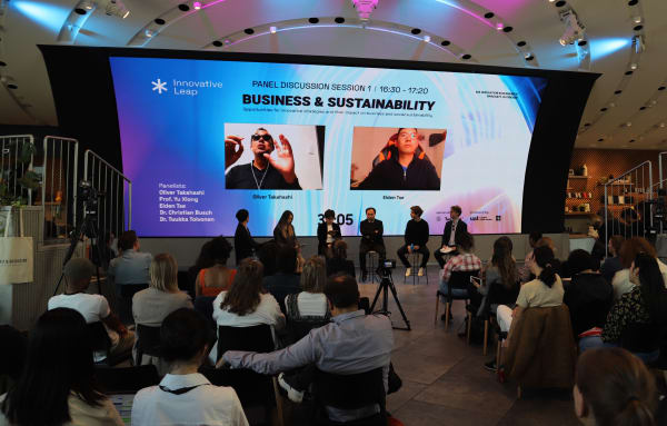 Panel sitting in front of an audience and large screen about business and sustainability