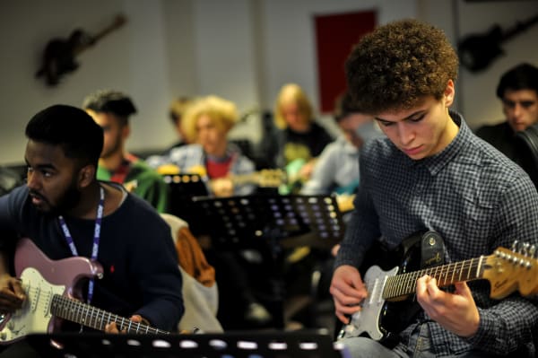 Image of two students playing the guitar in a class setting