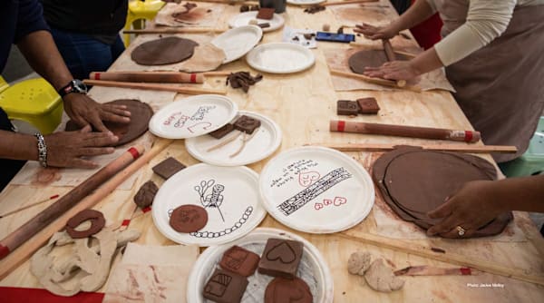 peoples hands gathered around a table making things out of clay and using art supplies