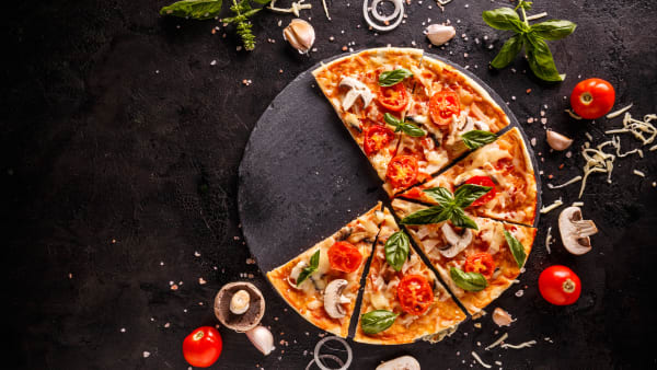 Pizza on a table with vegetables spread around it. 