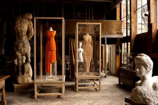 Dresses displayed in vitrines surrounded by shadowy statuary in a large room