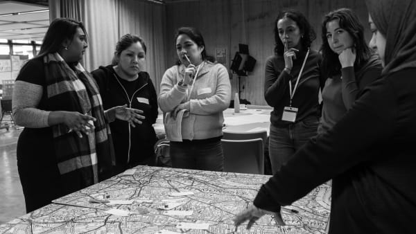 Several people from different backgrounds and ethnicities are around a table. On the table, there is a map.