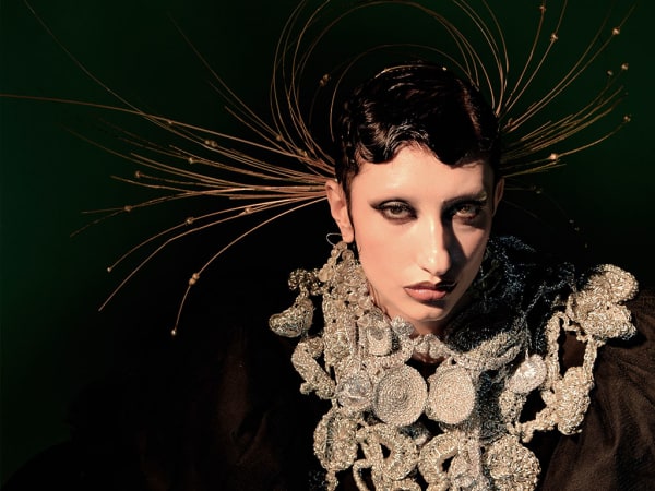 Female model in gold head dress, dark material and heavy gold material necklace.