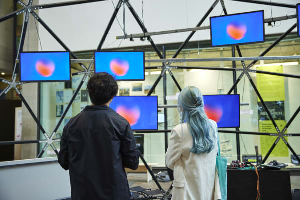 Two people face screens hangingi above them with blue backgrounds and red heart shapes