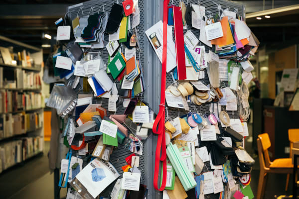 Close-up of a section of a square-shaped metal column with 2 sides visible. It is full of attached samples, badges and other colourful materials.