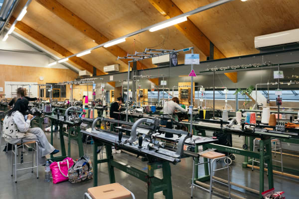 Students working at machinery in a large industrial knit workshop, including Dubied andflat knitting machines.