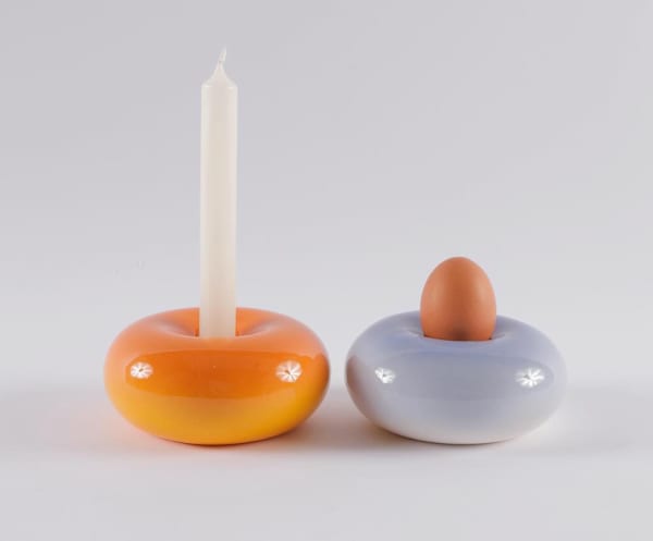 Orange and pale blue glazed ceramic designs that resemble ring doughnuts side by side, one holds a candle, the other an egg.