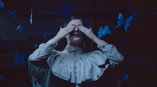 Female wearing red nail polish covering her eyes with herhands, surrounded by butterflies