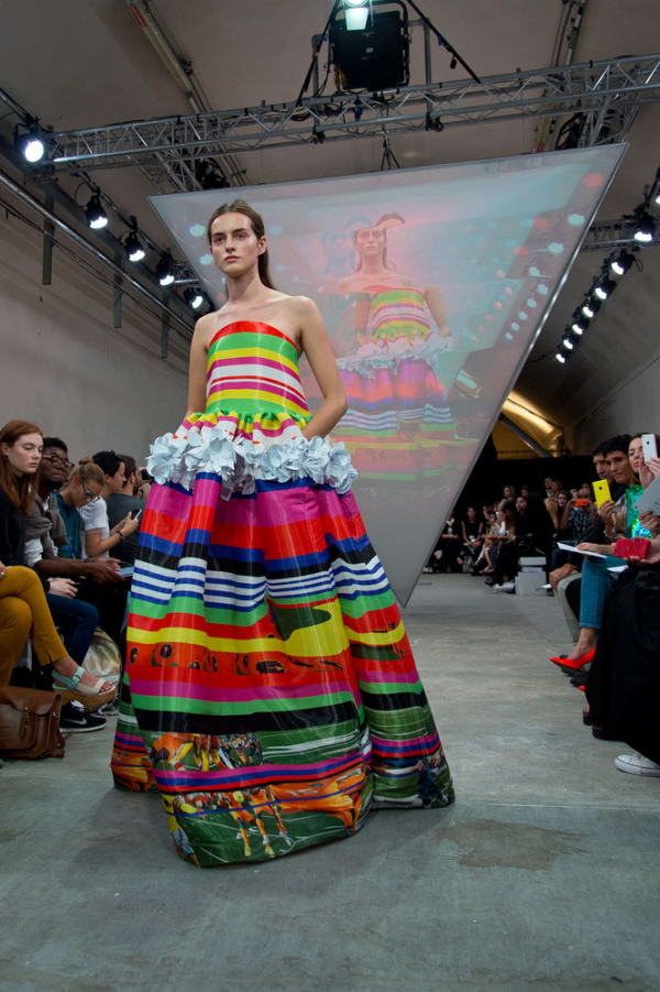 Model on catwalk wearing colourful dress - displayed on screen in background