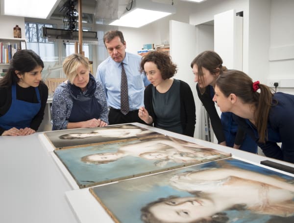 Group of people talking about a selection of oil paintings