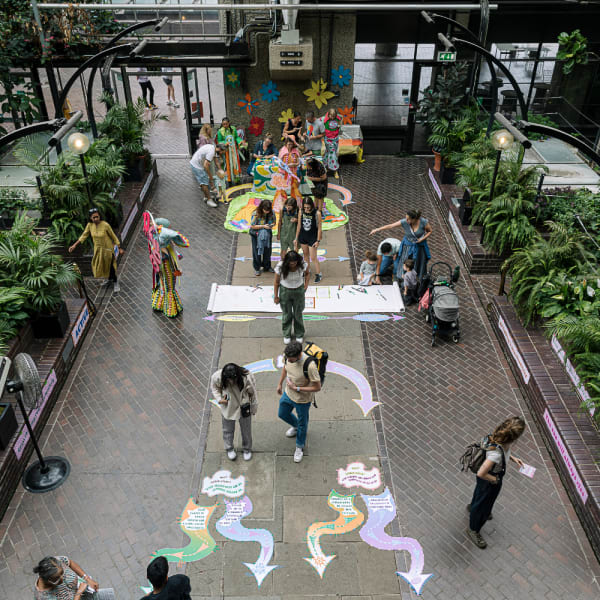 People walk along a path with information written on the floor. Plants line the path either side