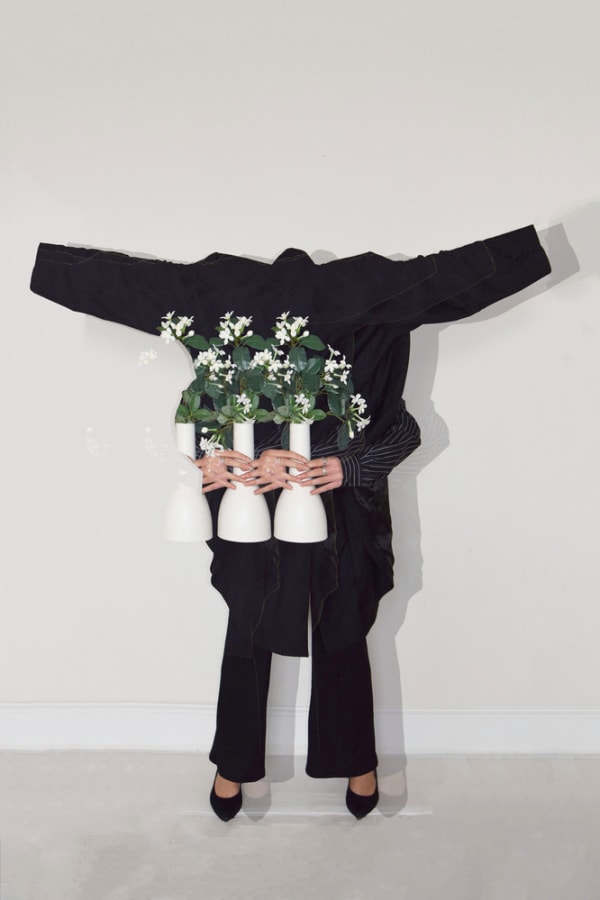 Dark suit standing with hands coming out from the waist holding 2 vases