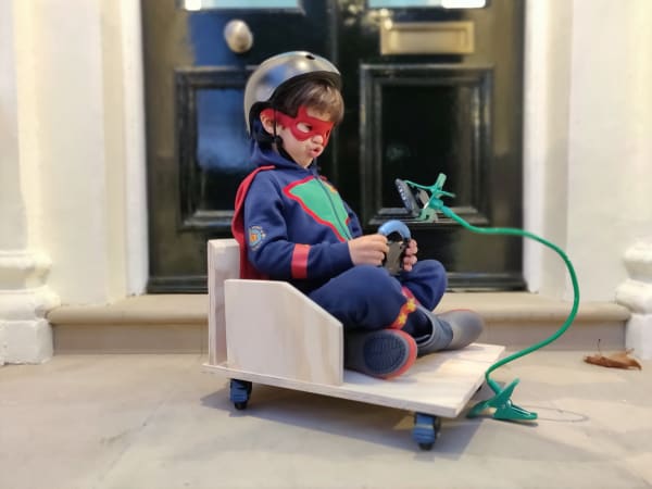 A kid in a wooden car wearing a superhero outfit and wired apparatus