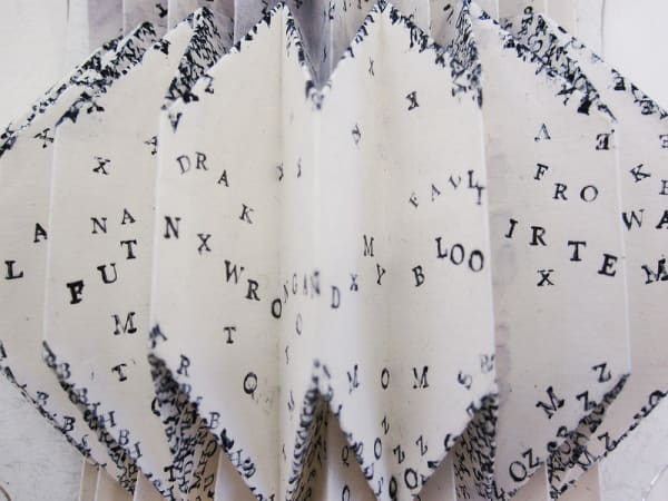 White, concertina paper object with scattered handprinted letters 