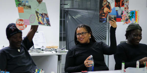Photograph of three students two of them are holding up pieces of paper with collages on them the other is smiling in the corner