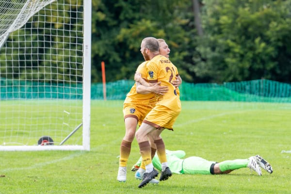 2 Sutton United players embrace after scoring a goal.