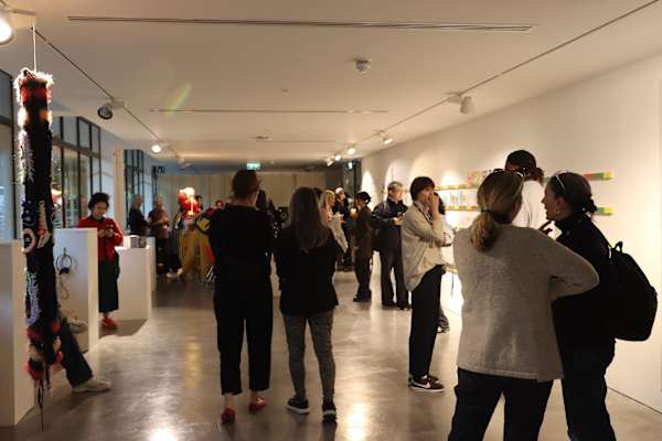 People gather in a modern gallery, engaging with vibrant wall art and sculptures. The atmosphere is lively and contemplative, fostering discussion.
