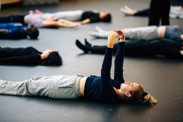 Performer in casual clothes lying on the floor with their arms stretched above them