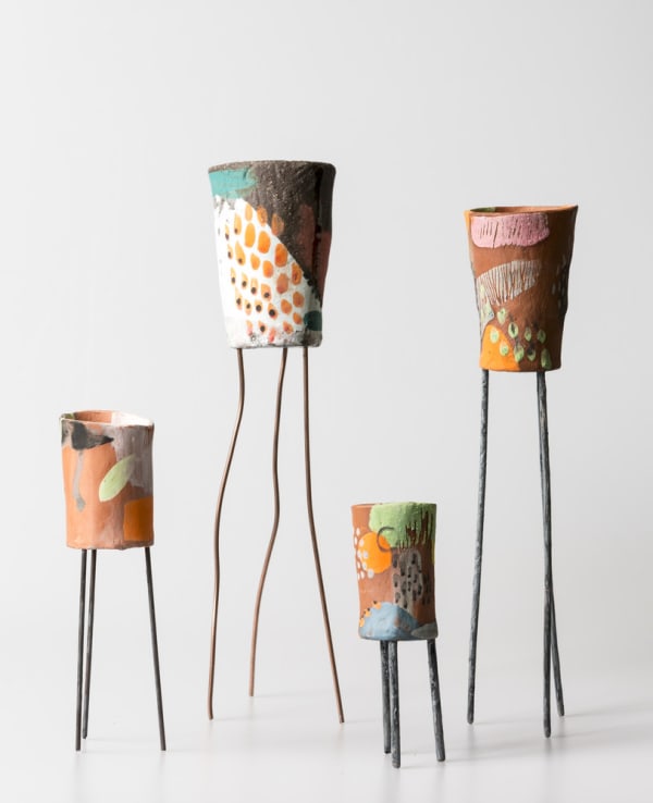 Four colourful ceramic vases each stone on three metal legs