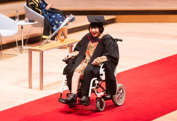 Graduate with assisted wheelchair getting across stage for graduation