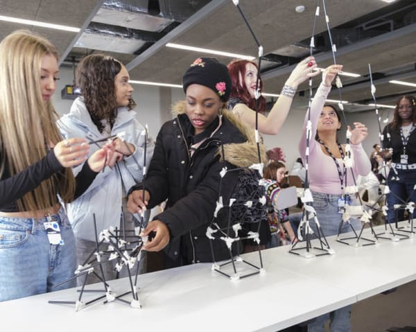 A group of students work together to construct a structure from paper straws and masking tape