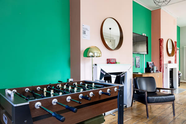 Common room featuring a foosball table, retro mirrors above the fireplace, and green and pink painted walls.