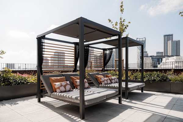 A rooftop terrace with grey cushioned sunbeads bordered by lavender planting and string lights, with a city skyline visible in the background.