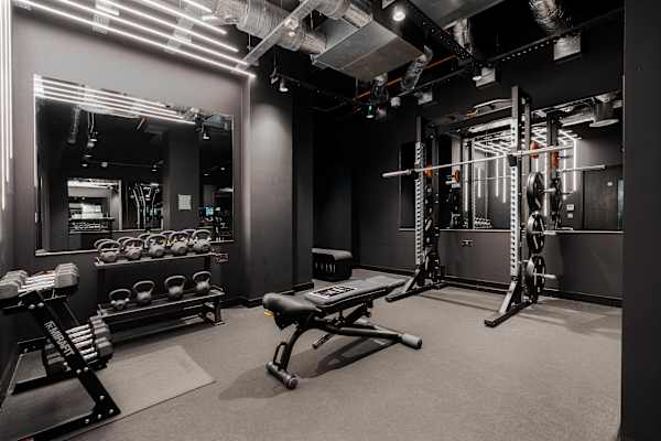 A dark grey gym with dark walls, weights, gym equiptment and a large mirror.