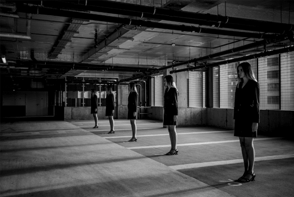 Black and white photograph of models standing in a line in a carpark-style building.