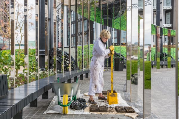 Woman making concrete blocks outside in a boiler suit standing in a mirrored walkway