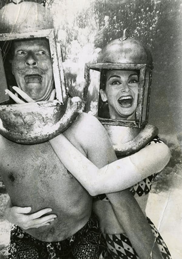aged desaturated black and white photo of Carmen and another model posed in an embrace underwater, both wearing diving helmets.